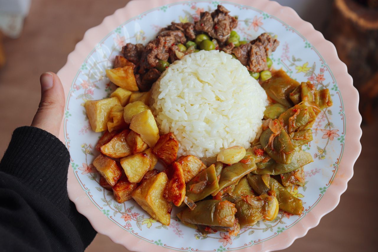 A close-up of a plate comprising white rice, roasted potatoes, sautéed green beans, and tender beef, offering a delicious meal.